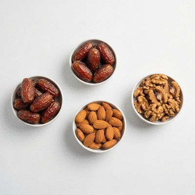 A balanced snack of dates paired with almonds and walnuts in small bowls on a clean white surface, no text, no words, no typography, clean image