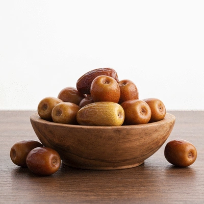 A bowl of fresh Khalas dates on a rustic wooden table, with soft, natural lighting