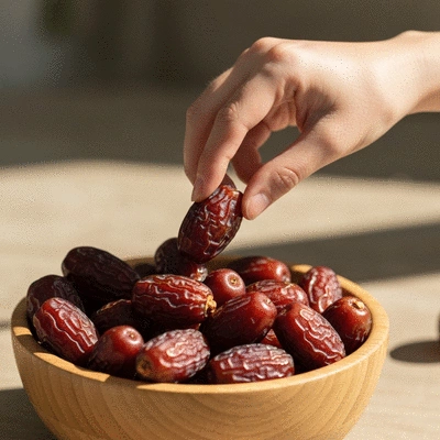 Hand reaching for a date from a beautifully arranged bowl of premium dates, implying fresh consumption